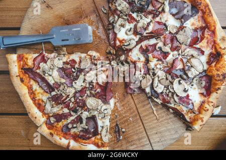 Nahaufnahme einer in Scheiben geschnittenen gebackenen Pizza auf dem Tisch zu Hause oder im Restaurant auf dem Brett Draufsicht Stockfoto