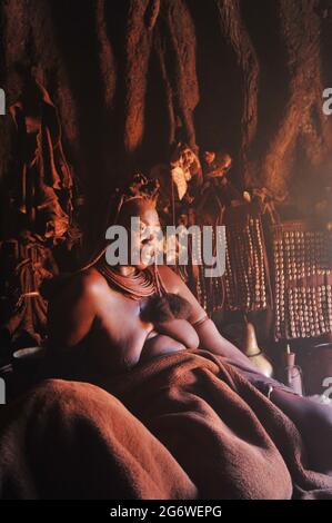 NAMIBIA. HIMBA-FRAU, DIE SICH IN IHRER HÜTTE AUSRUHTE. Stockfoto