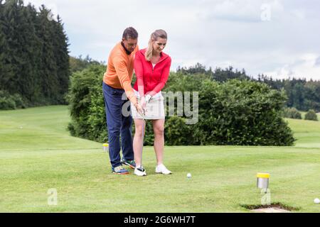 Mann, der Frau beibringt, Golf zu spielen, während sie auf dem Feld steht Stockfoto