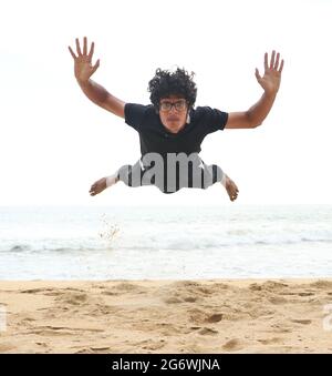 Mann, der nach einem Push-up an einem hellen Sommernachmittag auf den Sandstrand springt Stockfoto