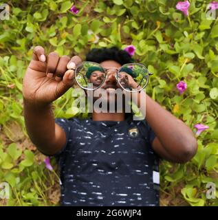 Das Gesicht einer Person, die durch seine Brille schaute, hielt sich auf ihm, während sie auf den grünen Pflanzen schlief Stockfoto