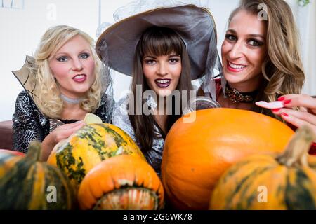 Lustig junge Frauen und beste Freunde teilen verschiedenen köstlichen Süßigkeiten während Halloween feiern gemeinsam im Kostüm Party im Innenbereich Stockfoto