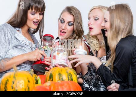 Lustig junge Frauen und beste Freunde teilen verschiedenen köstlichen Süßigkeiten während Halloween feiern gemeinsam im Kostüm Party im Innenbereich Stockfoto