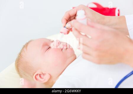 Nahaufnahme der Hände eines Kinderarztes, der die Nase eines Babys klärt, durch Anwendung von Kochsalzlösung in den Nasenlöchern mit einem Nasensauger während der Physica Stockfoto
