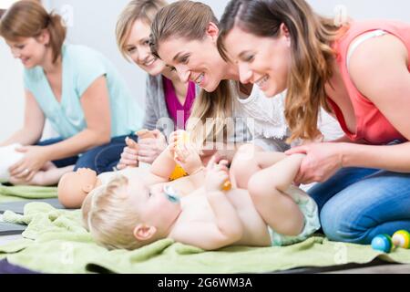 Eine Gruppe fröhlicher Frauen, die lernen, sich um ihre Babys zu kümmern, während der Elternstunde für junge Mütter in einem modernen Club für Mütter Stockfoto