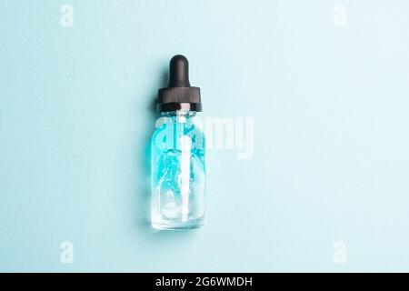 Kosmetisches Flüssiggel-Serumgleitmittel in einer transparenten Glasflasche mit einer Pipette auf blauem Hintergrund Stockfoto