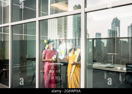 Drei indische Mitarbeiter haften Erinnerungen auf Glas Wand mit geschäftlichen Aufgaben und Termine im Büro Stockfoto