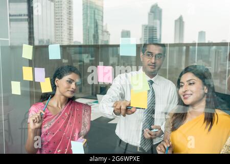 Drei indische Mitarbeiter haften Erinnerungen auf Glas Wand mit geschäftlichen Aufgaben und Termine im Büro Stockfoto