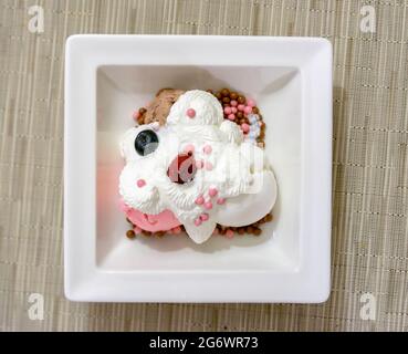 Blick von oben auf Vanille- und Erdbeereis mit Schlagsahne und Beeren, serviert auf einem weißen Dessertgericht, natürliches Licht. Stockfoto