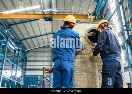 Zwei asiatische Arbeiter, die Isoliermaterial auf einen industriellen Dampfkessel auftragen Stockfoto