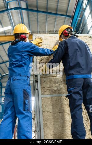 Zwei asiatische Arbeiter, die Isoliermaterial auf einen industriellen Dampfkessel auftragen Stockfoto