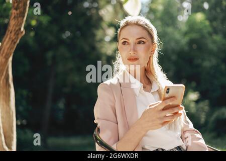 Erfolgreiche junge Geschäftsfrau, die im Café im Freien sitzt und das Smartphone benutzt Stockfoto