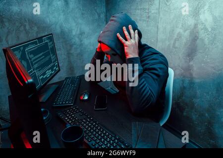 Anonymer Internet-Hacker mit Maske am Tisch sitzend und mit Computer Stockfoto