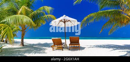 Wunderschöne tropische Insellandschaft, zwei Sonnenliegen, Liegen, Sonnenschirm unter Palmen. Weißer Sand, Meerblick mit Horizont, idyllisch blauer Himmel, Ruhe Stockfoto