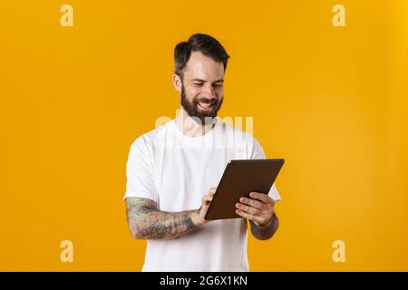 Glücklich mittleren Alters Brünette bärtigen Mann hält digitale Tablette über der gelben Wand stehen Stockfoto