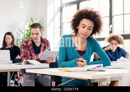 Junge Schülerin mit einem ernsten Gesichtsausdruck Konzentration beim Schreiben einen Aufsatz im Unterricht an einer internationalen Universität Stockfoto
