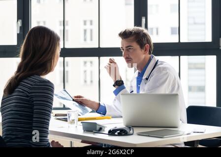 Junge gewidmet Arzt Holding eine X-ray beim Hören mit Aufmerksamkeit für seine weiblichen Patienten während einer privaten Beratung im Büro Stockfoto