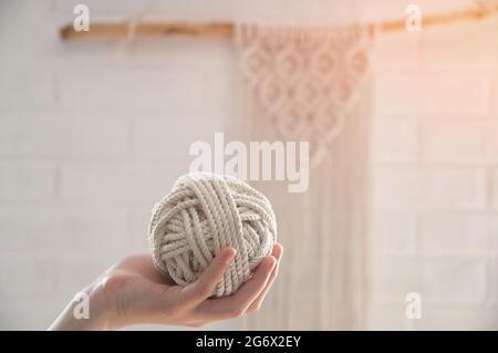 Der Garnknäuel zum Stricken von Makrame liegt auf der Hand vor dem Hintergrund einer weißen Wand Stockfoto