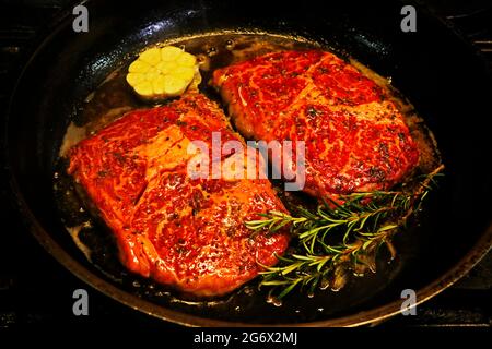 japanisches Wagyu-Rindersteak, das mit frischen Kräutern und Knoblauch in einer heißen Grillplatte zubereitet wird Stockfoto