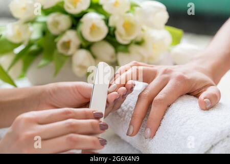 Nahaufnahme der Hand eines qualifizierten Maniküre Feilen der Nägel, einer jungen Frau mit einem weißen Puffer in einem trendy Nail Salon Stockfoto