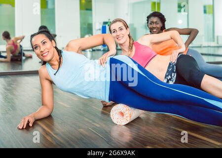 Schön freundlich lächelnden Frau beim Tragen von Blue Fitness ärmelloses top und Leggings während der Gruppe Training Klasse von Foam rolling an der Turnhalle Stockfoto