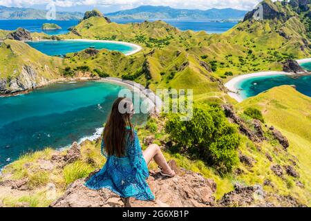 Rückansicht einer jungen Frau genießen die tolle Aussicht auf Padar Insel beim Sitzen auf der Oberseite ein vulkanischer Berg, während der Sommerferien in Indonesien Stockfoto