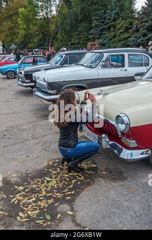 Dnipro, Ukraine - 06. Oktober 2013: Mädchen mit luxuriösen lockigen Haaren fotografiert Retro-Auto mit ihrem Smartphone auf einer Ausstellung von Oldtimern Stockfoto