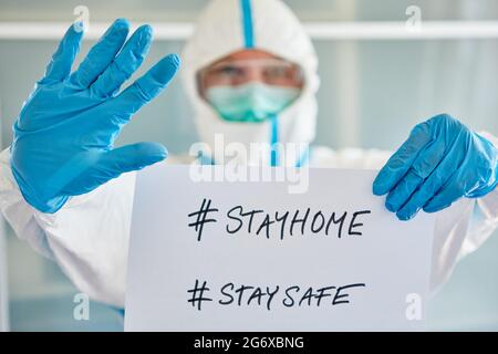 Krankheitskontrolle Mitarbeiter in Schutzkleidung mit #stayhome #staysafe notice wegen Covid-19 Pandemie Stockfoto