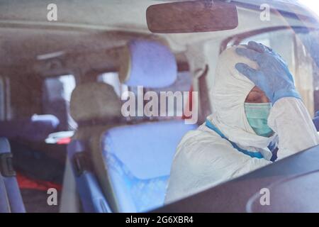 Erschöpfter Sanitäter in Schutzkleidung macht während der Coronavirus-Pandemie eine Pause im Krankenwagen Stockfoto
