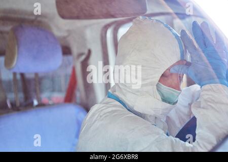 Müde Sanitäter im Krankenwagen in Schutzkleidung hinter dem Steuer macht eine Pause von Coronavirus-Pandemie Stockfoto