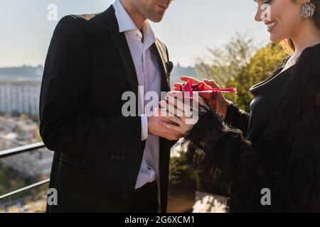 Mann, der einer fröhlichen Frau auf der Terrasse einen roten Geschenkkarton gab Stockfoto