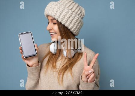Nahaufnahme Porträt Foto von schönen positiven fröhlich junge dunkelblonde Frau trägt beige stilvolle Pullover und gestrickten Hut tragen Kopfhörer und Stockfoto