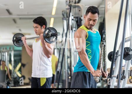 Junger Mann beim Trizeps-Pushdown am Seilzuggerät neben seinem Freund während des Oberkörpertrainings im Fitnessstudio Stockfoto