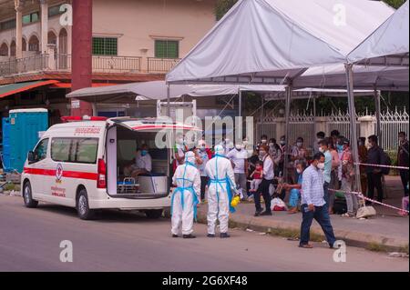 Phnom Penh, Kambodscha. 9. Juli 2021. Seit 4 Monaten kämpft Phnom Penh mit einem COVID - 19 Anstieg. Kambodschaner, die positiv auf das Virus getestet haben, warten auf einen Krankenwagen, mit verpackten Taschen, an einer Massenteststelle. 2 Notärzte/Sanitäter in voller PSA kontrollieren die Situation. Eine kambodschanische Mutter und ihr Baby haben beide positiv getestet und sind bereit, in die Ambulanz zu kommen. Kambodschaner, die positiv testen, können den Teststandort nicht verlassen und müssen einen Freund oder einen Verwandten anrufen, um ihre persönlichen Sachen für den 2-wöchigen Aufenthalt im Krankenhaus abzuholen. Quelle: Kraig lieb / Alamy Live News Stockfoto