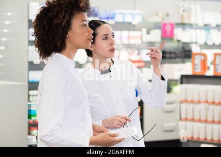 Seitliche Sicht auf zwei engagierte weibliche Apotheker suchen die beste Medizin im Lager beim zusammen in einer modernen Apotheke arbeiten Stockfoto