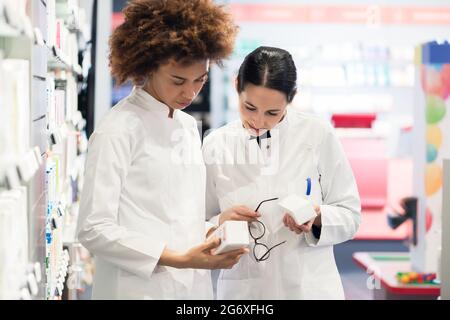 Seitliche Sicht auf zwei engagierte weibliche Apotheker suchen die beste Medizin im Lager beim zusammen in einer modernen Apotheke arbeiten Stockfoto