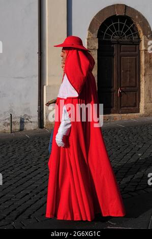 Ein Mann in einem prächtigen rot-weißen Kardinalkostüm schlendert mit einer fein gekleideten Dame auf der Piazza Guglielmo Marconi in Anagni, Latium, Italien, bei einem historischen Festzug im August, der an seine Vergangenheit als Stadt der Päpste erinnert, Das Sommerrefugium zwischen dem 11. Und 14. Jahrhundert der Päpste, die ihre relative Kühle der schwellenden Hitze Roms vorzogen. Anagni war auch der Geburtsort der Päpste Gregory IX und Boniface VIII. Stockfoto