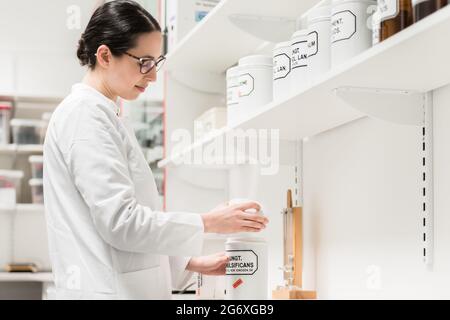 Seitenansicht einer erfahrenen Apothekerin, die den Behälter einer chemischen pharmazeutischen Substanz während der Inventur in einer modernen Drogerie überprüft Stockfoto