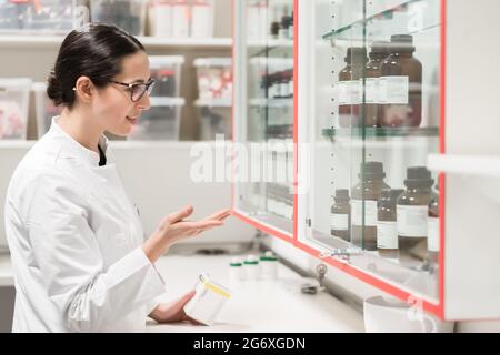 Seitenansicht einer erfahrenen Apothekerin, die den Behälter einer chemischen pharmazeutischen Substanz während der Inventur in einer modernen Drogerie überprüft Stockfoto