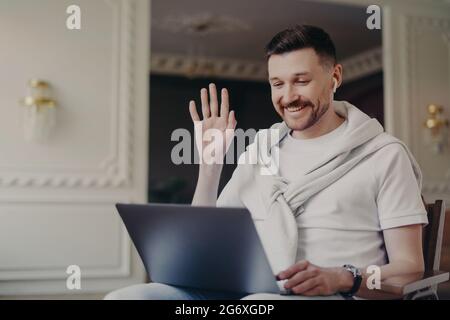 Porträt eines Geschäftsmannes oder Freiberuflers, der jemanden über einen Laptop begrüßt, während er zu Hause auf einem Stuhl sitzt Stockfoto
