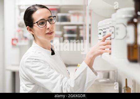 Seitenansicht einer erfahrenen Apothekerin, die den Behälter einer chemischen pharmazeutischen Substanz während der Inventur in einer modernen Drogerie überprüft Stockfoto