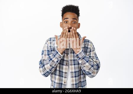 Der überraschte afroamerikanische Mann starrt in Ehrfurcht, keucht erschrocken, hält die Hände auf den Lippen, bedeckt den Mund vor Schock, hört Offenbarung, steht erstaunt Stockfoto