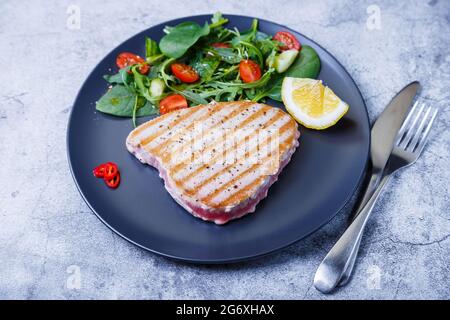 Gegrilltes Thunfischsteak mit frischem Gemüse, Rucola, Spinat und Zitrone. Nahaufnahme. Stockfoto