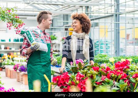 Fröhliche stattlichen Arbeiter tragen einen Sack Blumenerde beim Gespräch mit einem schönen weiblichen Kunden in einem modernen Flower Shop Stockfoto