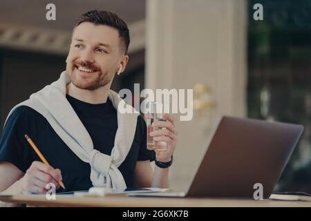 Ein gutaussehender Geschäftsmann in legerer Kleidung mit einem Glas Wasser, der im modernen Büro arbeitet Stockfoto