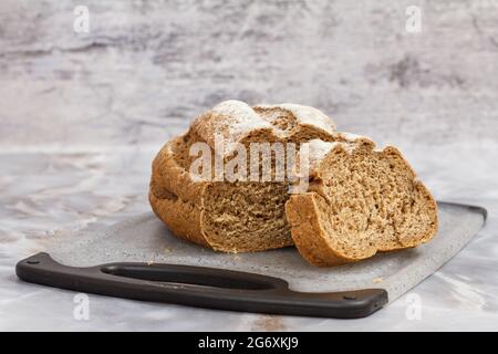 Geschnittenes Brot auf Schneidebrett auf Küchentischtisch mit grauem Hintergrund Stockfoto