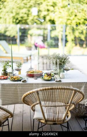 Der Tisch im Garten ist mit einer Tischdecke bedeckt und mit Blumen und Kerzen mit Essen für zwei Personen geschmückt. Abendessen im Sommer im Freien. Stockfoto