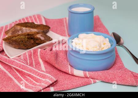 Quark in einer blauen Schüssel mit Sauerrahm und Honig. Geröstetes Brot auf einem Teller. Frühstück am Morgen. Stockfoto