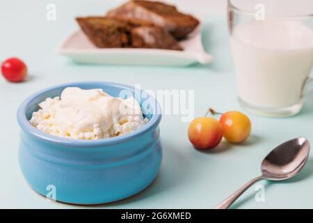 Quark in einer blauen Schüssel mit Sauerrahm und Honig. Geröstetes Brot auf einem Teller. Frühstück am Morgen. Stockfoto