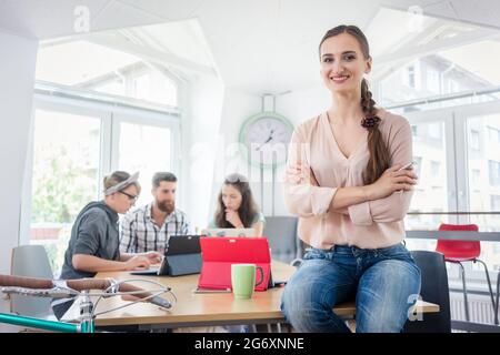 Porträt eines erfolgreichen Unternehmer mit Blick auf die Kamera, während er auf dem Schreibtisch in der Shared Office Space in einem Hub für unabhängige Auftragnehmer Stockfoto
